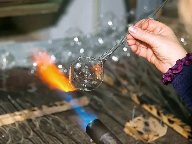Glassblower heats the glass piece for shaping the future Christmas ornament