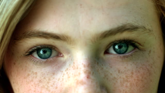 A CloseUp Of A Young Woman's Eyes, She Stares Into Camera, Then Her Eyes Brighten As She Smiles