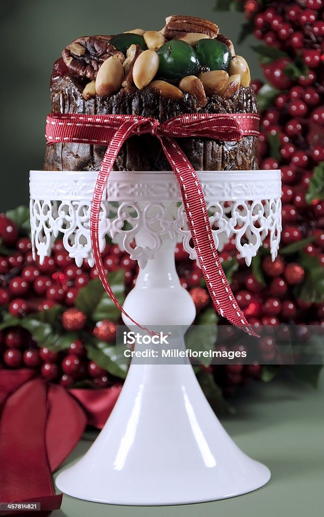 Festive Christmas fruit cake with glace cherries and nuts Festive Christmas food, fruit cake with glace cherries and nuts on white cake stand with holiday berry wreath in green background. Selective focus. Cakestand Stock Photo