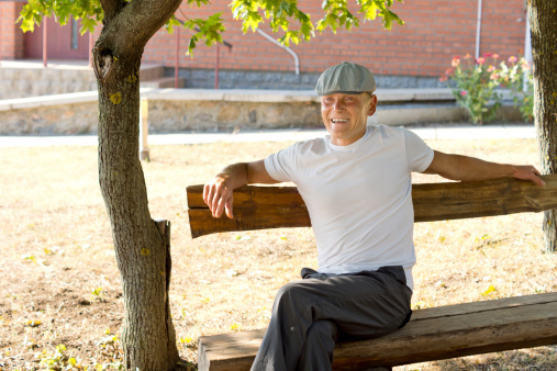 Middle-aged Caucasian man smiling while sitting on a bench in a sunny day of summer