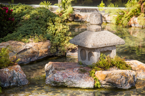 Japanese lantern made out of carved stone in water.