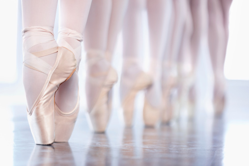Cropped shot of a group of ballerinas standing in a row with their feet 