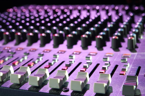 Sound mixer button in concert, with faders button to set the volume, and lights from the stage. Focus on faders on foreground.