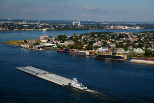 Tug pushing a barge going around Algiers Point on the Mississippi River in New Orleans,  Louisiana with Bywater, Holy Cross and Lower Ninth Ward in the background.