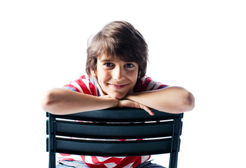 Cute, happy young boy with red and white shirt sitting on a chair smiling. Isolated on white background