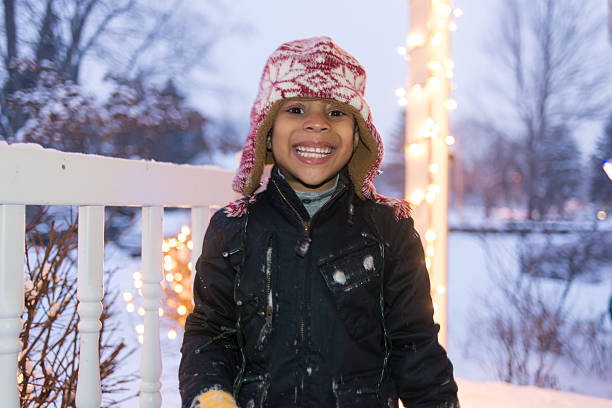 Portrait of a young black boy after he has been playing in the snow with Christmas lights in background.