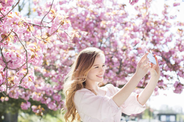 istock Woman taking self-portrait under tree with pink blossoms 457979775