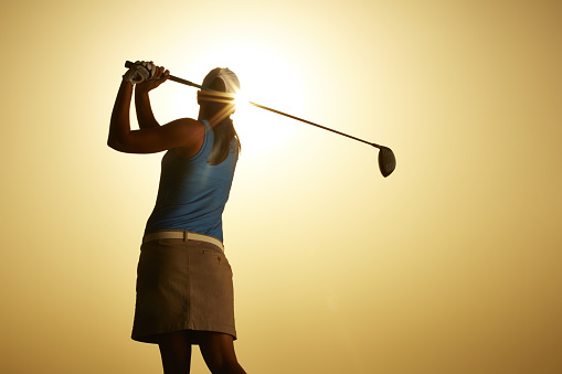 Sun shining behind woman swinging golf club