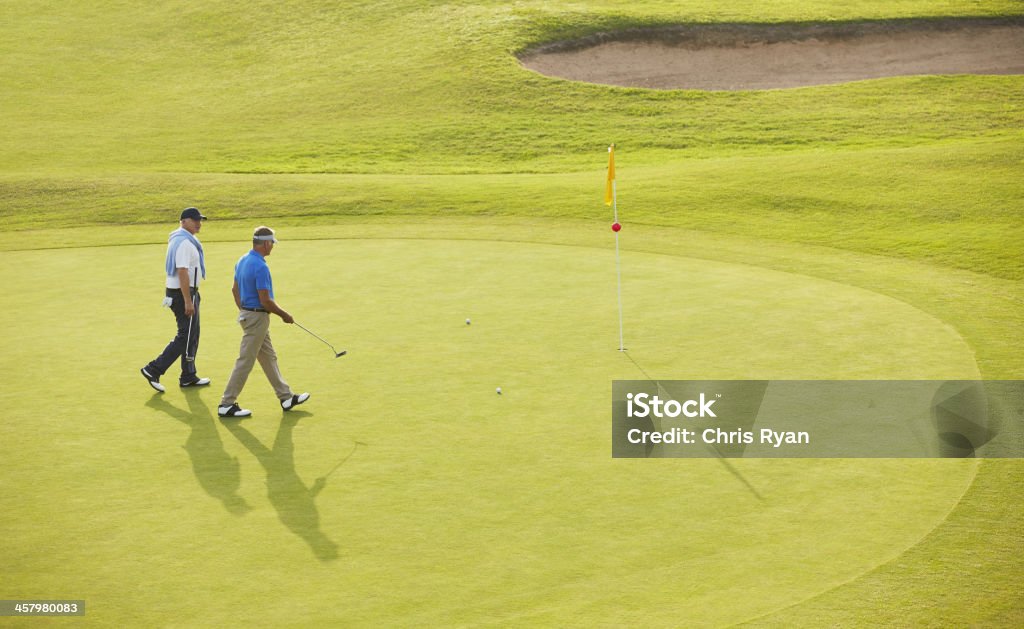 Senior men walking toward flag and hole on golf course  Golf Stock Photo