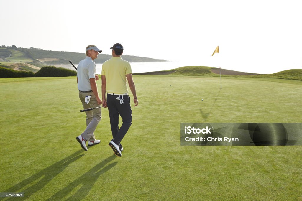 Men walking toward hole on golf course overlooking ocean  Golfer Stock Photo