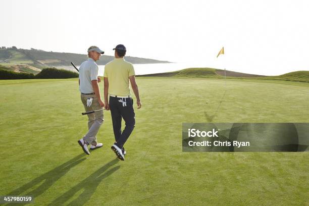 Men Walking Toward Hole On Golf Course Overlooking Ocean Stock Photo - Download Image Now