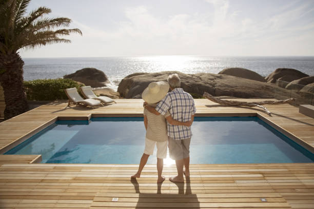 senior coppia abbracciare dalla moderna piscina con vista sull'oceano - wealth foto e immagini stock