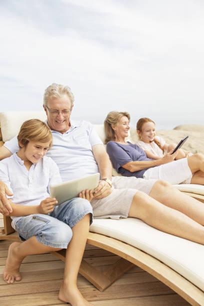 grands-parents et petits-enfants à l'aide de tablette numérique au bord de la piscine - reading beach e reader men photos et images de collection