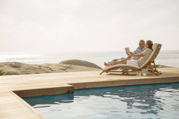 older couple relaxing by pool - senior adult couple computer retirement 뉴스 사진 이미지