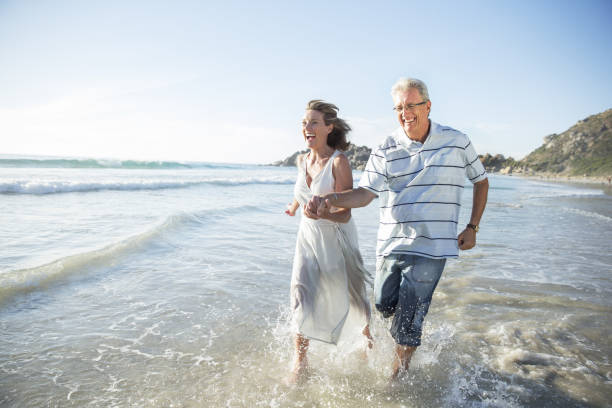 Older couple playing in waves on beach  60 69 years stock pictures, royalty-free photos & images