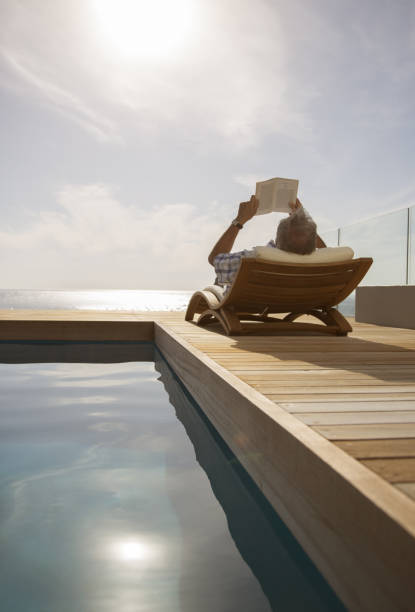 istock Man reading in lawn chair by pool 457981235