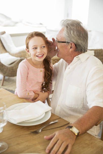 anziani uomo e nipote sussurrare al tavolo - whispering grandparent child grandfather foto e immagini stock