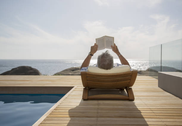 hombre mayor leyendo junto a la piscina - lying on back fotos fotografías e imágenes de stock