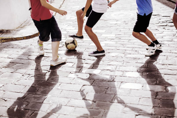 niños jugando con pelota de fútbol en alley - three boys fotografías e imágenes de stock