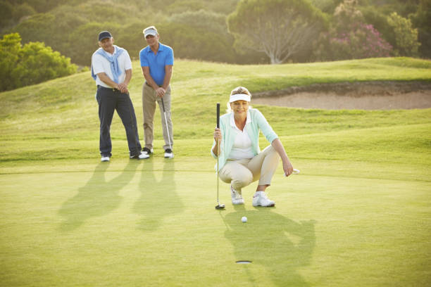 senior friends playing golf on course - putting together стоковые фото и изображения