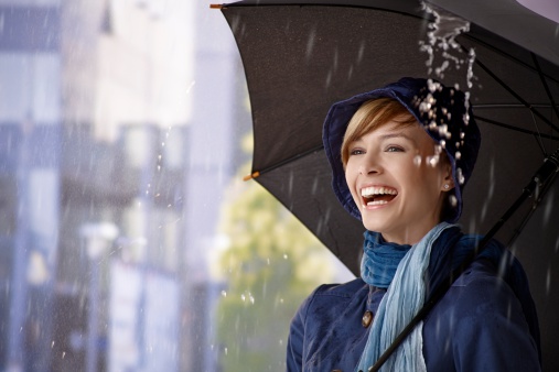 Happy young woman standing under umbrella in rain, laughing..