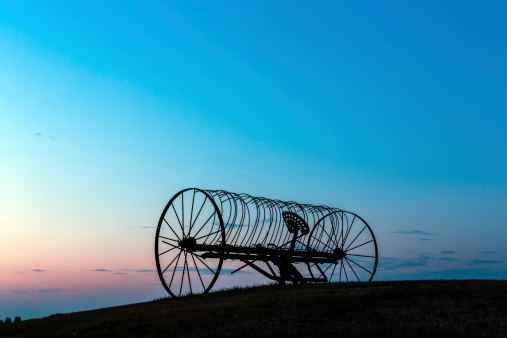 An old antique farm machine sitting on top of a hill at sunset