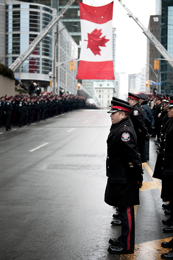 Toronto, Canada - January, 18 2011: Police Officers lined along downtown Toronto street in ceremonial uniform beneath the Canadian flag, which is suspended from the ladders from two fire engines.