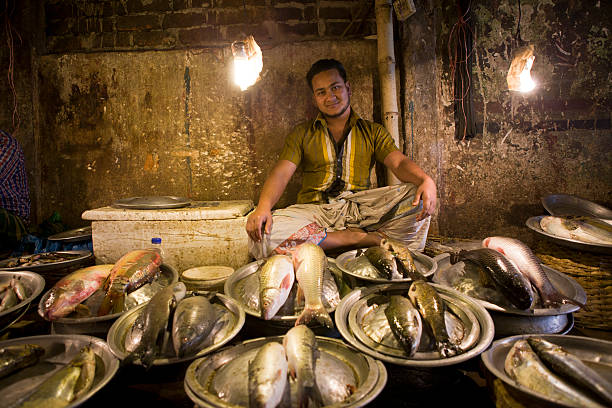 Young Man Selling Fish in a Market "Sylhet, Bangladesh - February 2, 2012: A young man selling fish. Fish is one of the main food for the people in Bangladesh." sylhet stock pictures, royalty-free photos & images