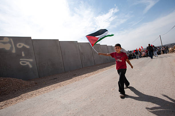 Palestinian Nonviolent Activism "AL-WALAJA, OCCUPIED PALESTINIAN TERRITORIES - November, 13 2010: A boy waving a Palestinian flag marches in a nonviolent protest against the Israeli separation barrier which threatens to encircle the West Bank town of Al-Walaja." apartheid sign stock pictures, royalty-free photos & images