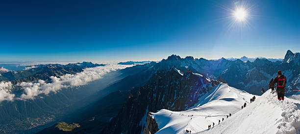 Mountaineers climbing above the clouds Alps panorama "Chamonix, France - July 1st, 2011: Alpinists carefully picking their way down the precipitous snow arete from the Aiguille du Midi into the Vallee Blanche on Mont Blanc as the early morning sun burns off the clouds above the Chamonix valley below. Composite panoramic image created from seven contemporaneous sequential photographs." aiguille de midi photos stock pictures, royalty-free photos & images