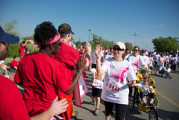Encouragement "Fort Worth, Texas, United States - April 9, 2011: A group of spectators (in red) cheer on walkers and runners just before the finish line during the Fort Worth 2011 Susan G. Komen Race for the Cure. The race is a major fundraiser for Susan G. Komen for the Cure which promotes breast health and cancer research." walking for a cause stock pictures, royalty-free photos & images