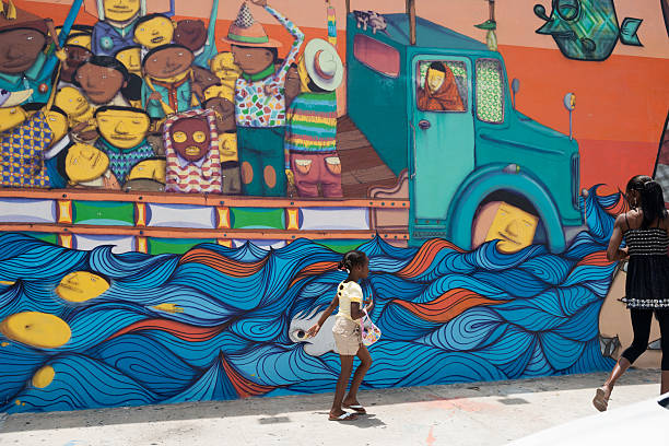 Young Caucasian woman artist painting sidewalk mural. She is dressed in casual work clothes. Exterior of public sidewalk in downtown of large North American City.