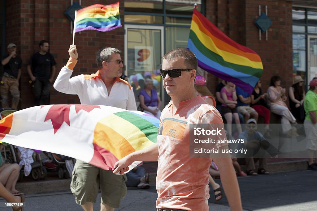 Men Carrying Rainbow Pride Flags "Halifax, Nova Scotia Canada - July 28, 2012: A young man with a Rainbow Canada flag walks in the Halifax Pride Parade. A man carrying a Rainbow Pride flag can also be seen marching in the background.  This year marked the 25th anniversary of the Pride celebrations in Halifax, Nova Scotia, Canada. People watching the parade can also be seen in the photo." 2012 Stock Photo
