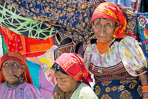 Kuna Indian Ladies "Mamardup Village, San Blas Islands, Panama - April 21, 2007: Group of three elderly Kuna Indian women smoking pipe and wearing Brightly colored traditional Mola fabrics and red Headscarves." loin cloth stock pictures, royalty-free photos & images