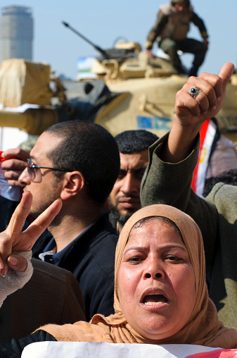 Cairo, Egypt - February 2, 2011: Several days into the 18 days of anti-government demonstrations that would lead to the resignation of President Hosni Mubarak, pro-Mubarak demonstrators were mobilized for a counter-demonstration. Here a woman stands with a group of men; in the background is an Egyptian soldier on a tank.