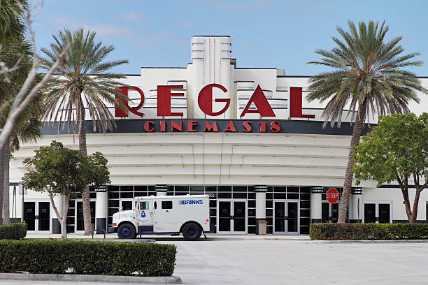 Regal Cinemas with Brinks truck making pickup "West Palm Beach, Florida, USA - February 14, 2011: A Regal Cinemas buidling with a Brinks armored truck parked in front of the building making a money pickup. This is a Regal 18 screen cinemaplex with Art Deco architecture framed by palm trees." armoured truck stock pictures, royalty-free photos & images