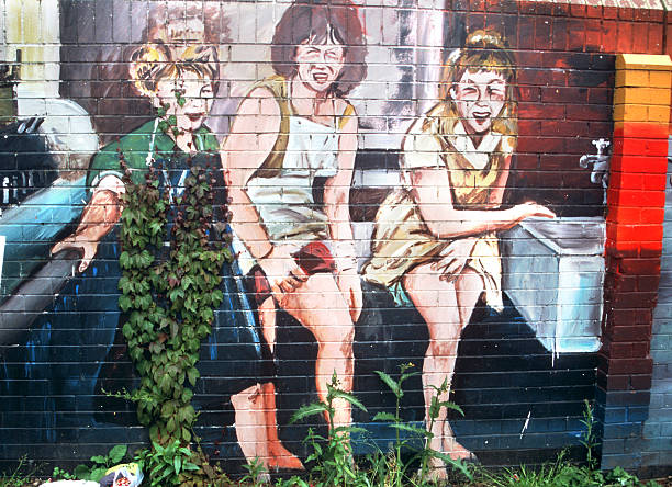 Female artist painting mural on public building wall.  She is dressed in casual work clothes. Exterior of urban cityscape of Toronto, Ontario in Canada. Drone point of view.