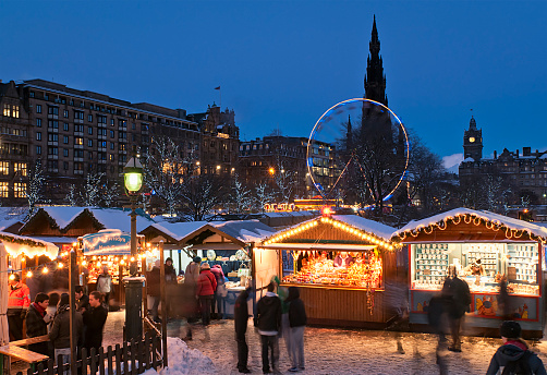 Edinburgh, Scotland - 1st December 2010: Shoppers visiting traditional wooden stalls at a public Christmas market situated next to Princes Street in the city centre of Edinburgh, with Jenners department store, the Scott Monument and the Balmoral Hotel visible on the skyline.