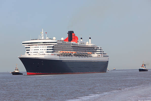 Queen Mary 2 "Liverpool,United Kingdom - September 15, 2011: Cunard's Ocean Liner Queen Mary 2 in the River Mersey approaching Liverpool with Mersey tugs following her.The ocean liner can carry 3056 passengers and 1253 crew and is 1132 feet long.She weighs 151400 tons and has 17 decks .Built for the Southampton to New York transatlantic trade,she also does a round the world cruise once a year.Liverpool is the historic home of Cunard." round the world travel stock pictures, royalty-free photos & images