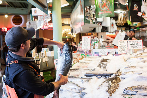 Pike Place Fish Market "Seattle, USA - May 17, 2012: Pike Place Fish Market.  One of the fishmonger is preparing to throw the fish at the popular Pike Place tourist market." pike place market stock pictures, royalty-free photos & images