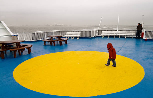 At sea, North Sea - May 16, 2011: on the DFDS' King Seaways ship, off Ijmuiden, Netherlands, it is cold, and this child is warmly dressed to walk on the top deck. The Dutch coast is visible on the horizon