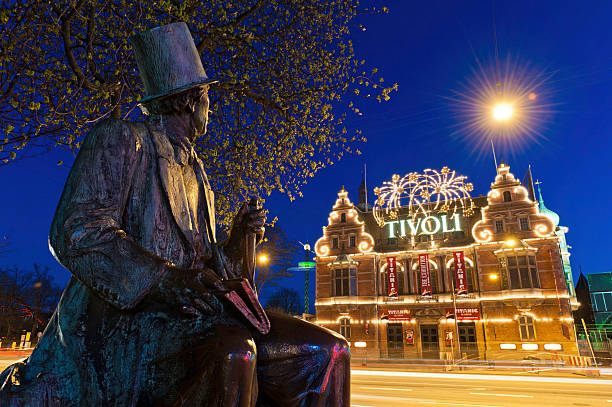 Copenhagen Hans Christian Anderson Tivoli Gardens Denmark "Copenhagen, Denmark - April 17th, 2011: Historic statue of Hans Christian Andersen, the famous Danish storyteller, looking over the ornate entrance to H C Andersen Slottet with its illuminated Tivoli Gardens amusement park sign at night in the RÃ¥dhuspladsen, City Hall Square." statue of hans christian andersen stock pictures, royalty-free photos & images