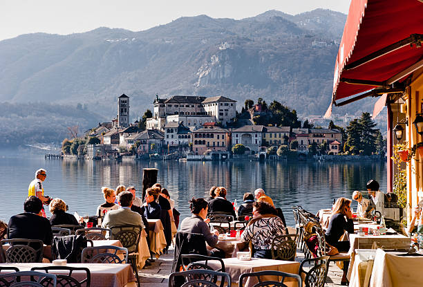 Summertime in Italy "Lake Orta, Italy - February 24, 2012: People enjoy lunch in a lakeside restaurant. With the nearby Unesco site Sacro Monte and San Giulio island, Orta is a popular destination for small-scale tourism." como italy photos stock pictures, royalty-free photos & images