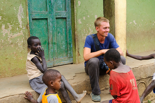 Jinka, Ethiopia - August 14, 2010: A young male European traveler in Africa, holding his digital SLR, sits with several Ethiopian boys while visiting the famous Saturday market.