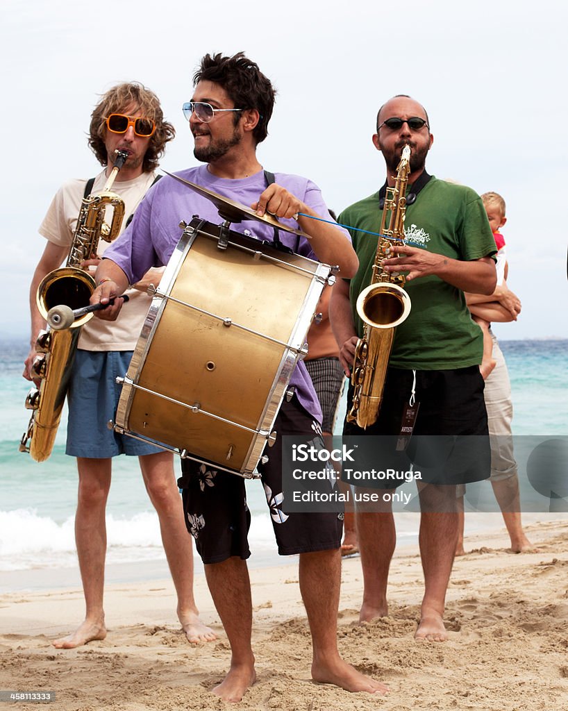 Italian Marching Band performing on the Beach in September "Santa Teresa Di Gallura, Italy - September 2, 2012: Italian Marching Band performing on the Beach of Reana Bianca.  Three barefoot players are entertaining the tourists during the jazz festival 'Musica sulle bocche'On the background two adults and a young boy attending the show." Drummer Stock Photo