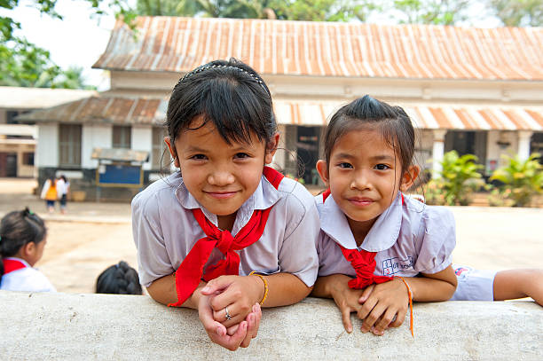 Two young children enjoy their time outdoors in Kratie Province, Cambodia. One child stands on a bench while the other sits on the ground, both surrounded by scattered bricks.