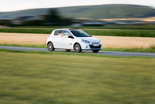 Wiesbaden, Germany - June 26, 2011: A middle-aged woman in an accelerating white Renault Clio III on a country-road near Wiesbaden, Germany on a sunny evening. Renault Clio is a supermini car designed and produced by the French car manufacturer Renault since 1990. Renault S.A. is a French car manufacturer producing cars, and trucks and was founded in 1899. Some motion blur.