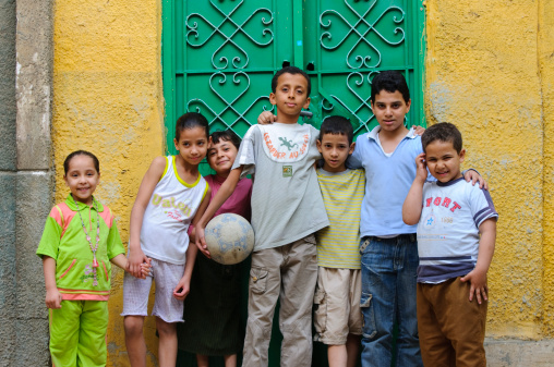 Cairo, Egypt - April 29, 2010: Egyptian boys and girls stand outside of their home with a soccer ball, about to play in the street. They live in the Northern City of the Dead, a part of Cairo filled with medieval tombs and mausoleums.