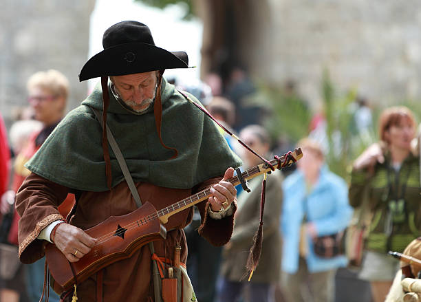 Medieval troubadour "Nogent le Rotrou, France- May, 16th, 2010: A medieval troubadour tunning his traditional string instrument during Week-end de L\'ascension-Grand Fete medievale in Nogent de Rotrou. This was a historical reenactment festival around the Saint Jean Castle." troubadour stock pictures, royalty-free photos & images