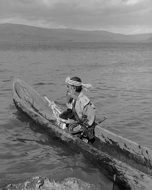 Ainu man. "Akan, Hokkaido, Japan - October 8, 1961: Ainu man in hand carved boat on Lake Akan, Akan National Park. Ceremonial attire for celebrating the Marimo (green moss ball), festival." national park akan stock pictures, royalty-free photos & images